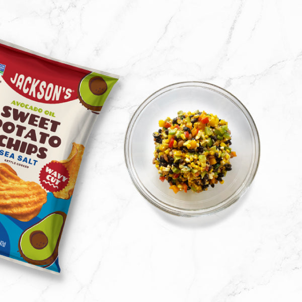 Bowl of cowboy caviar next to a bag of Jackson's Wavy Sea Salt Sweet Potato Chips