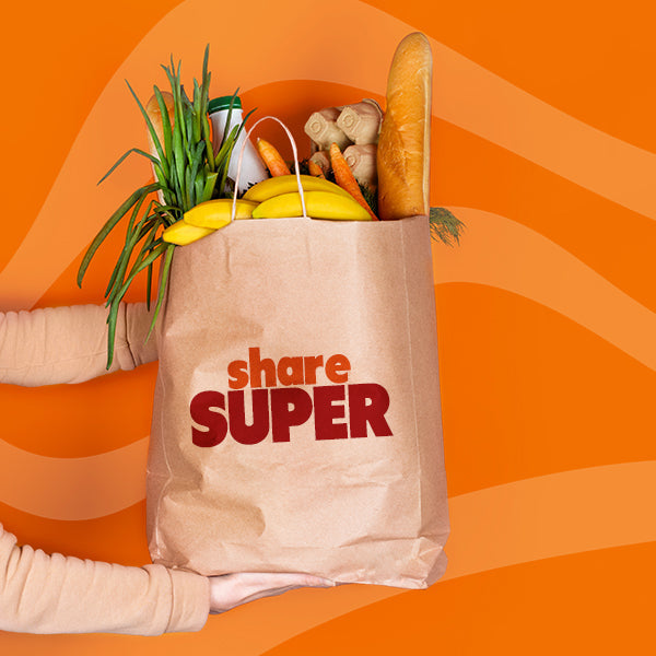 grocery bag with produce and snacks on orange background