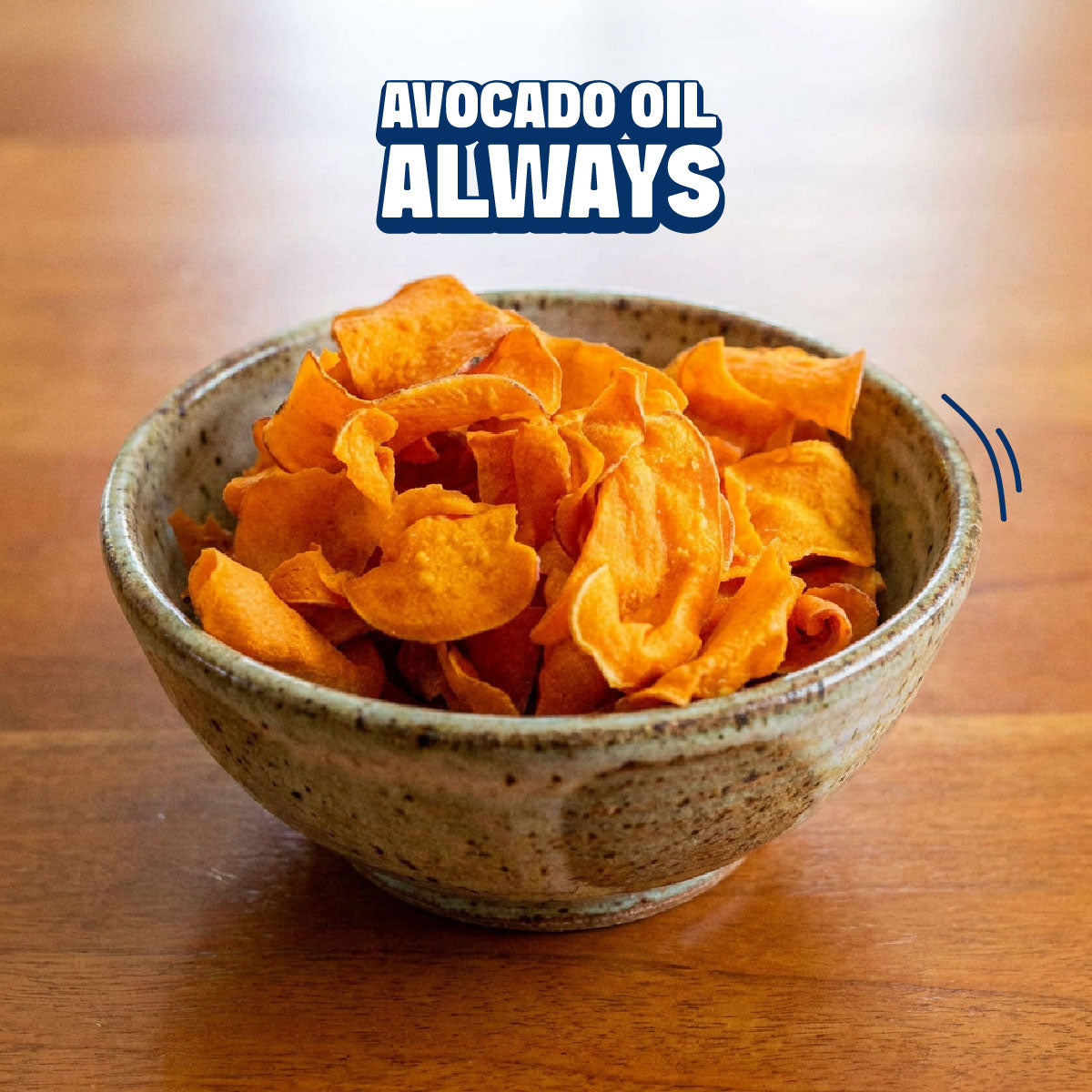 A ceramic bowl filled with golden-brown potato chips on a wooden table, with the text 'AVOCADO OIL ALWAYS' overlaid at the top.