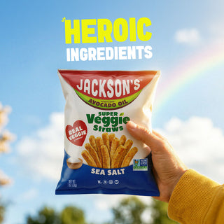 A hand holding a bag of Jackson's Super Veggie Straws Sea Salt in front of a bright blue sky with a rainbow and the text 'HEROIC INGREDIENTS' at the top.