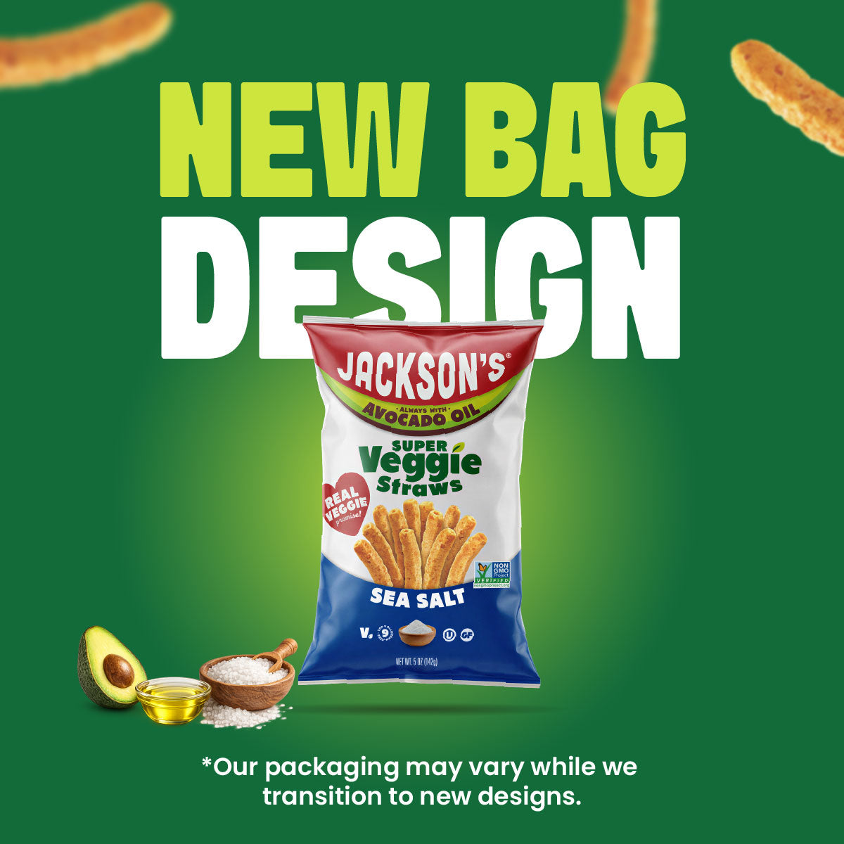 A bag of Jackson's Avocado Oil Super Veggie Straws Sea Salt snack stands on a green promotional background with large text reading 'NEW BAG DESIGN.' The package is white with red, yellow, and blue branding, and small food props including an avocado, a bowl of salt, and a small jar of oil appear near the lower left.