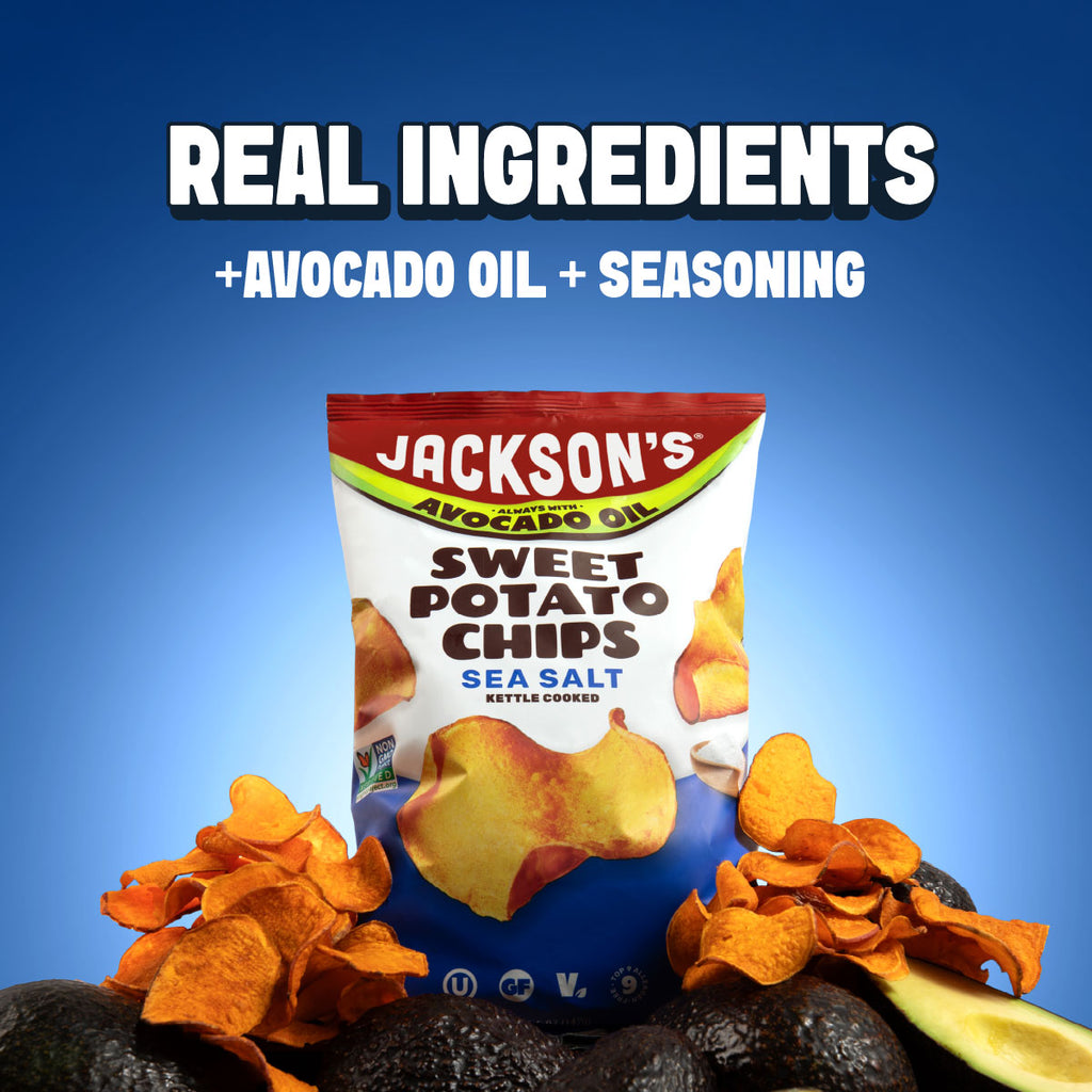 A bag of Jackson's Sweet Potato Chips Sea Salt Kettle Crusted is centered against a blue gradient background with promotional text reading 'REAL INGREDIENTS +AVOCADO OIL + SEASONING'. Sliced avocado, potato, and orange potato chips are arranged around the bag.