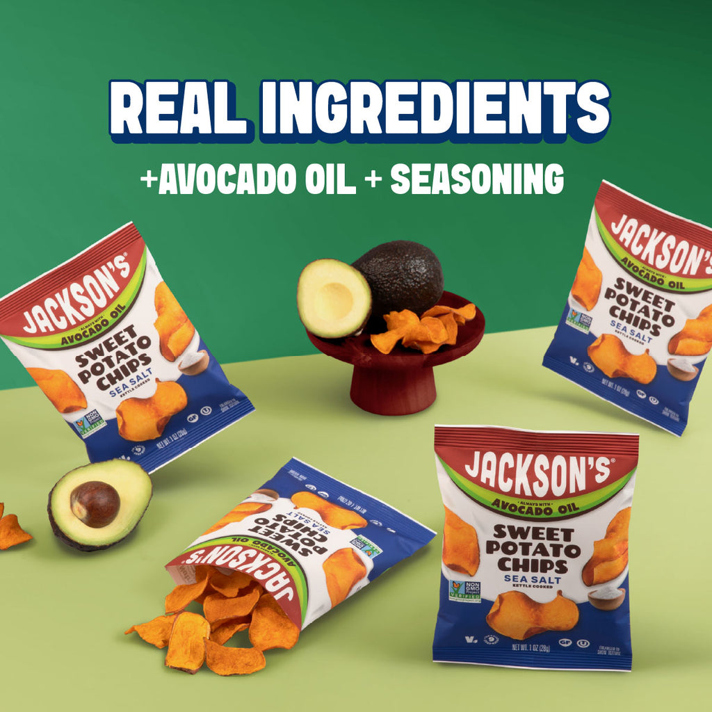 Four bags of Jackson's Sweet Potato Chips in avocado oil, sea salt flavor, arranged on a green and pale yellow surface with whole and sliced avocados and loose chips. Large text at the top reads 'REAL INGREDIENTS +AVOCADO OIL + SEASONING'.