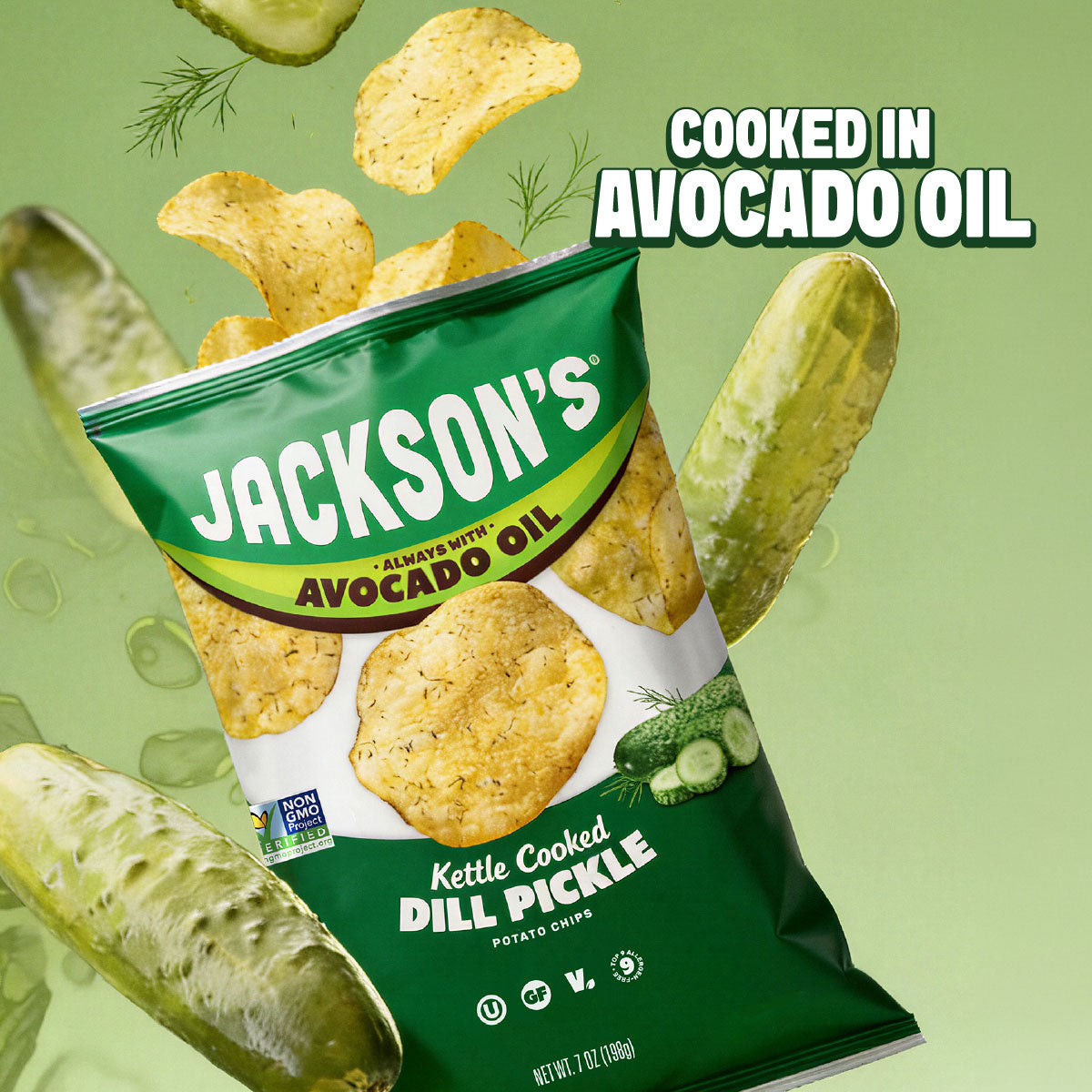 A bag of Jackson's Kettle Cooked Dill Pickle potato chips floating among illustrated whole cucumbers on a light green background, with the text 'COOKED IN AVOCADO OIL' at the top right.