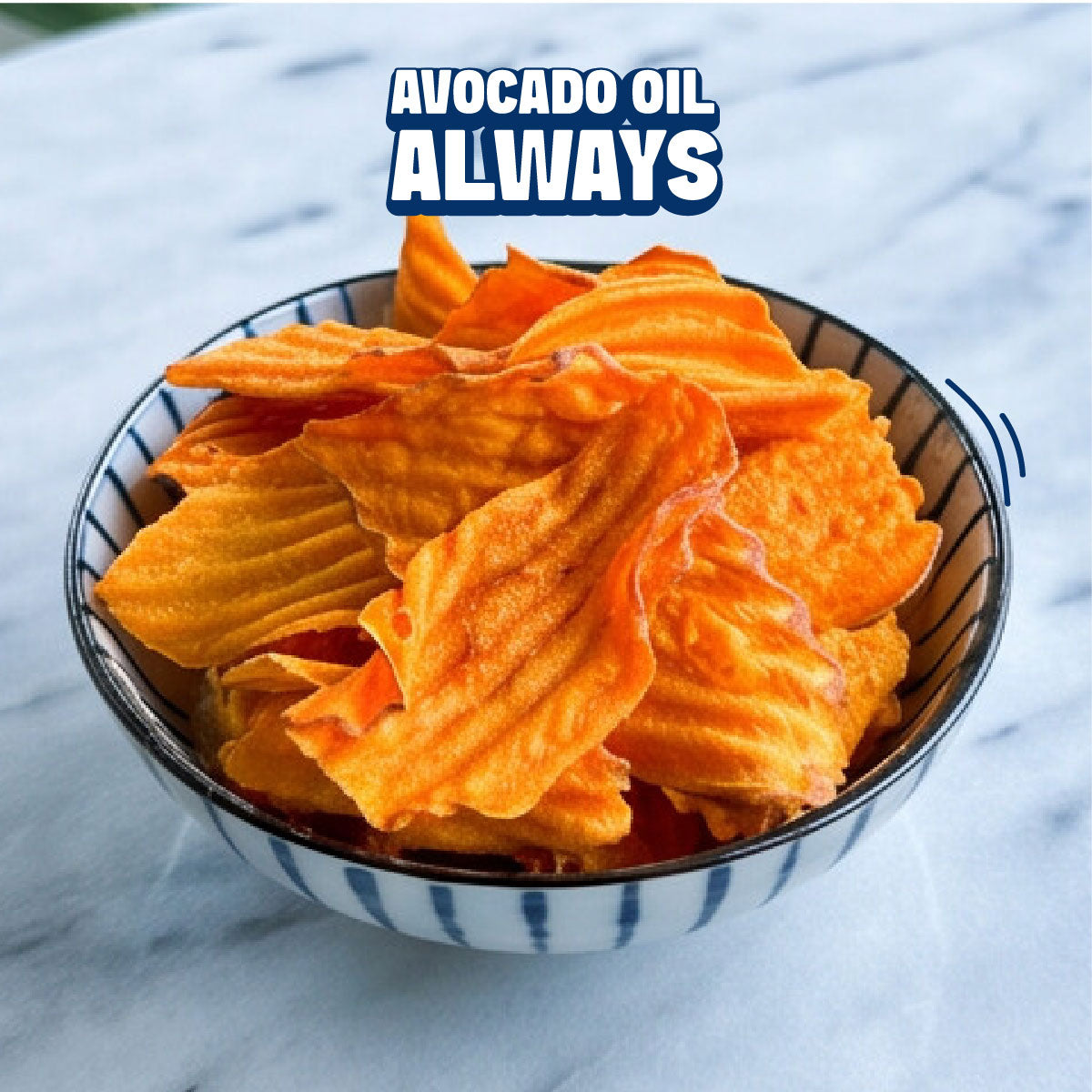 A bowl of golden-brown potato chips filled with orange avocado oil, set on a white marble surface with a text overlay that reads 'AVOCADO OIL ALWAYS'.